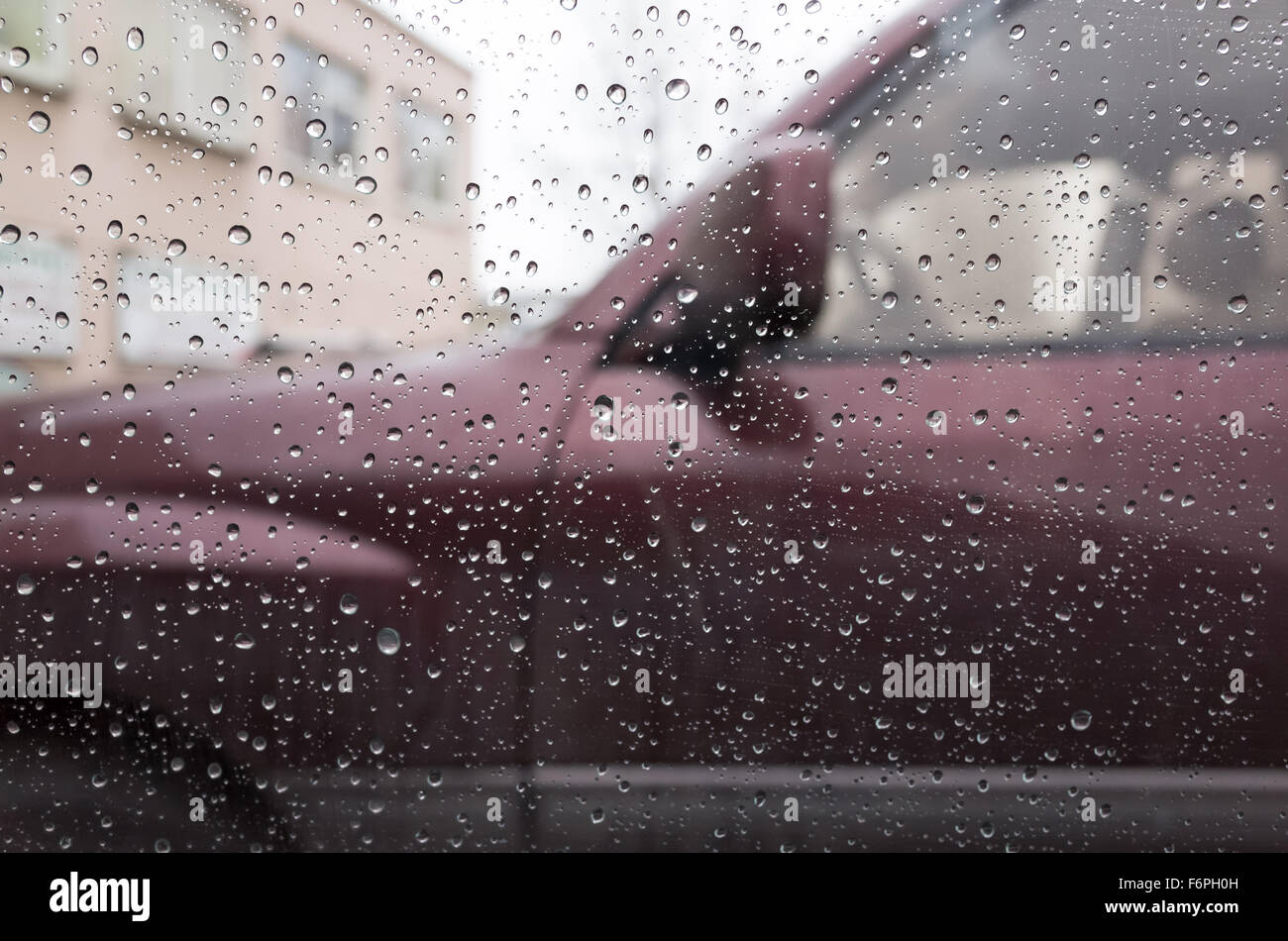Wet car window with raindrops and a blurred car behind. Closeup photo with selective focus and shallow DOF Stock Photo