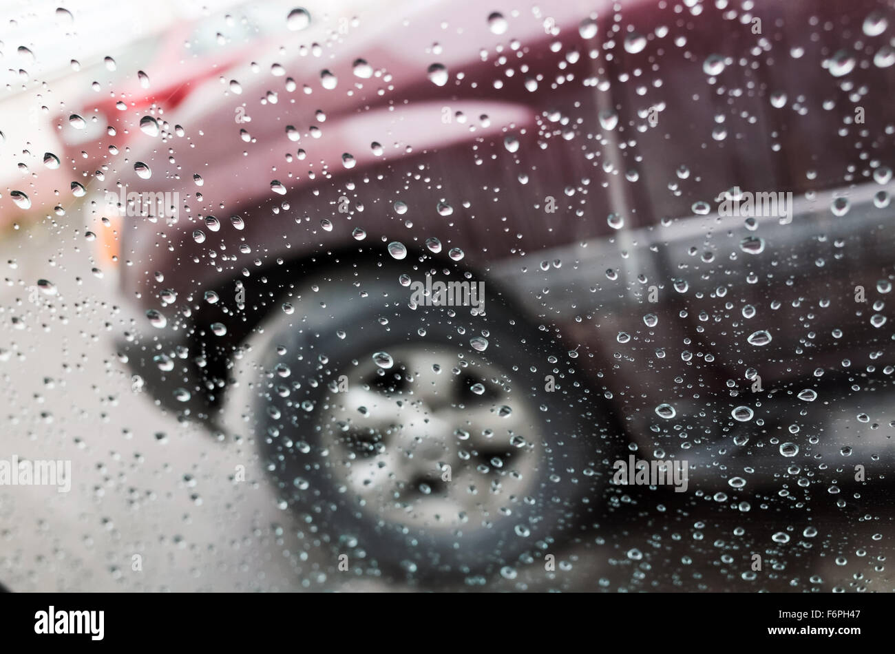 Wet car window with raindrops and a blurred car behind. Close-up photo with selective focus and shallow DOF Stock Photo