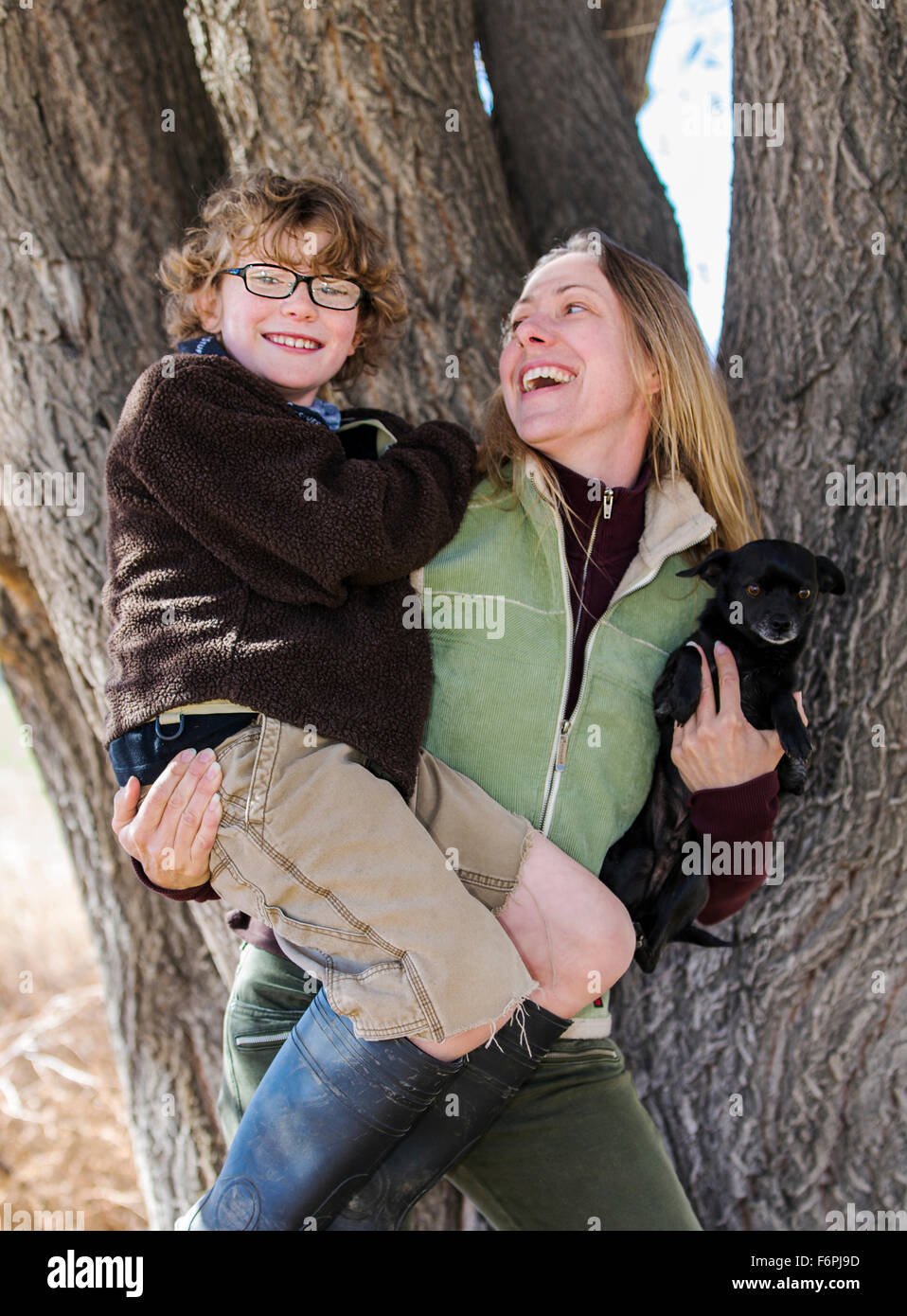 Attractive mother and young son pose with pet dogs for photographs by tree on ranch Stock Photo