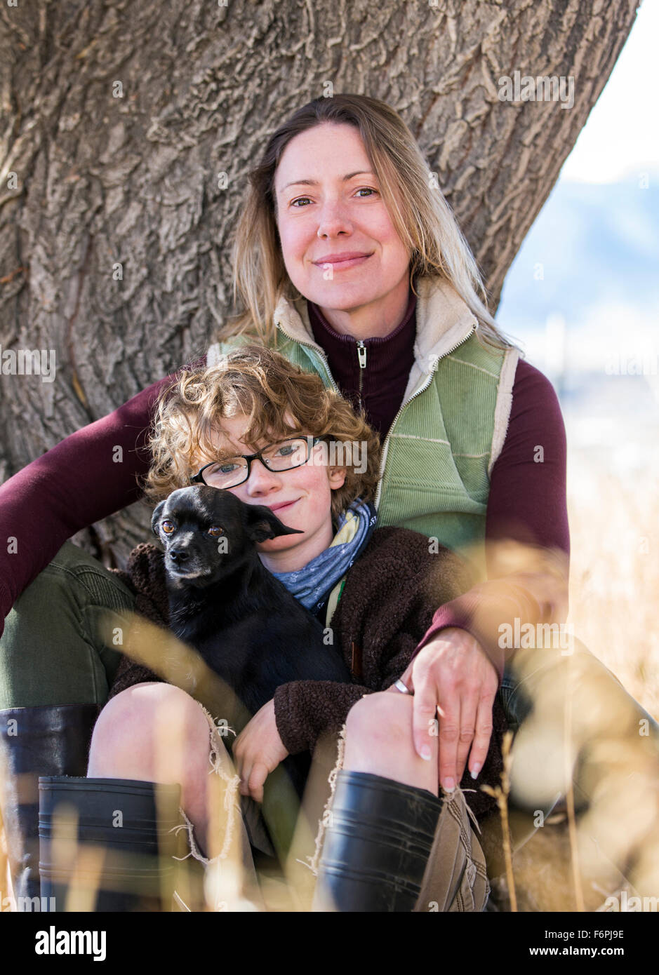 Attractive mother and young son pose with pet dogs for photographs by tree on ranch Stock Photo