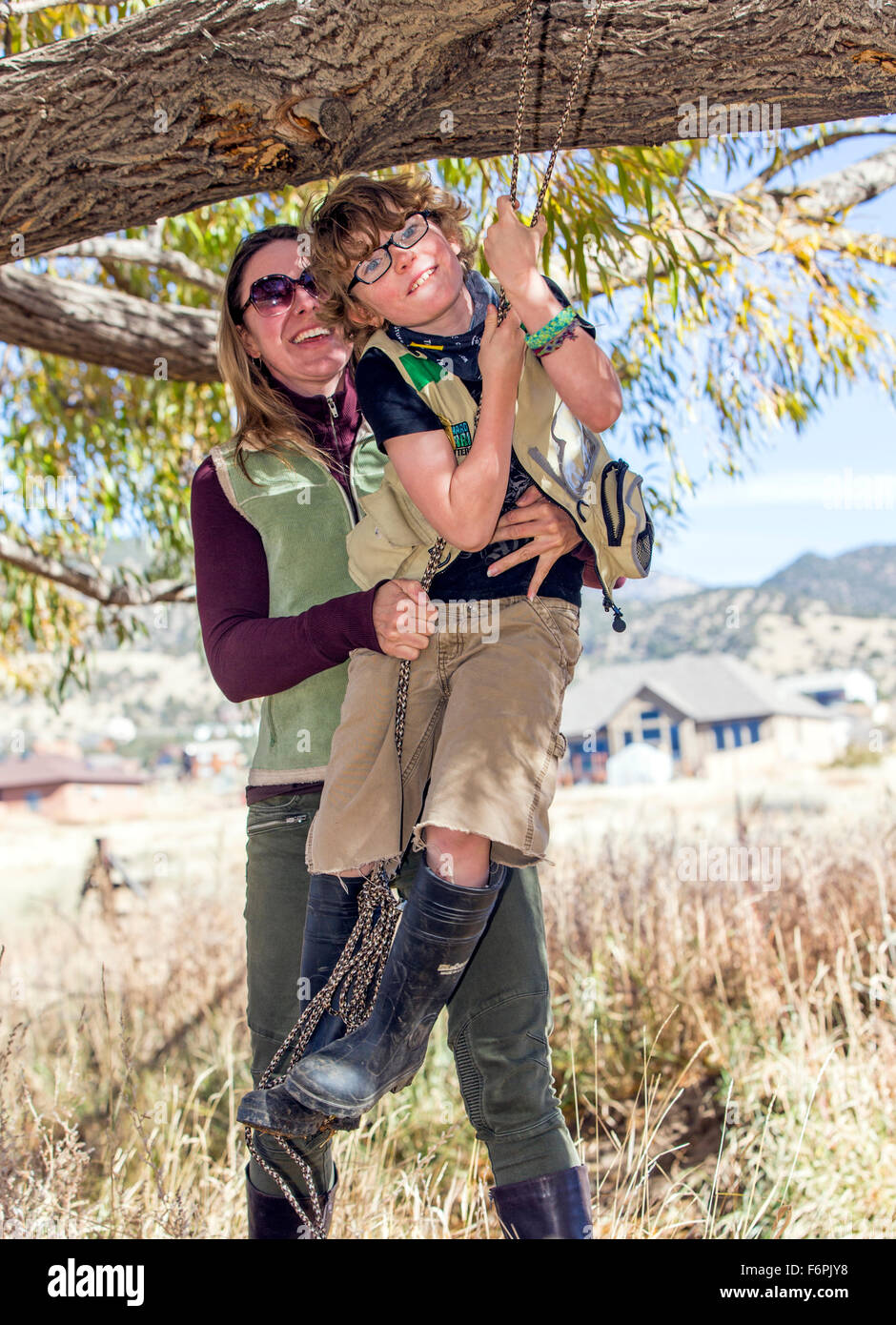Attractive mother helps young son on rope swing hung from ranch tree Stock Photo