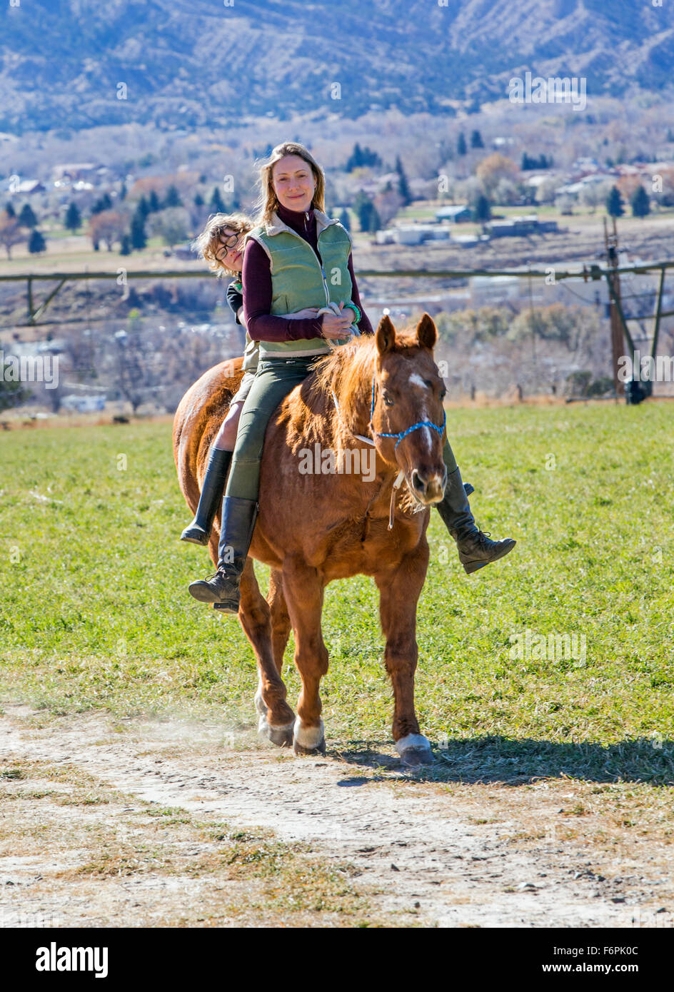 Attractive mother and young son riding horse in ranch pasture Stock Photo