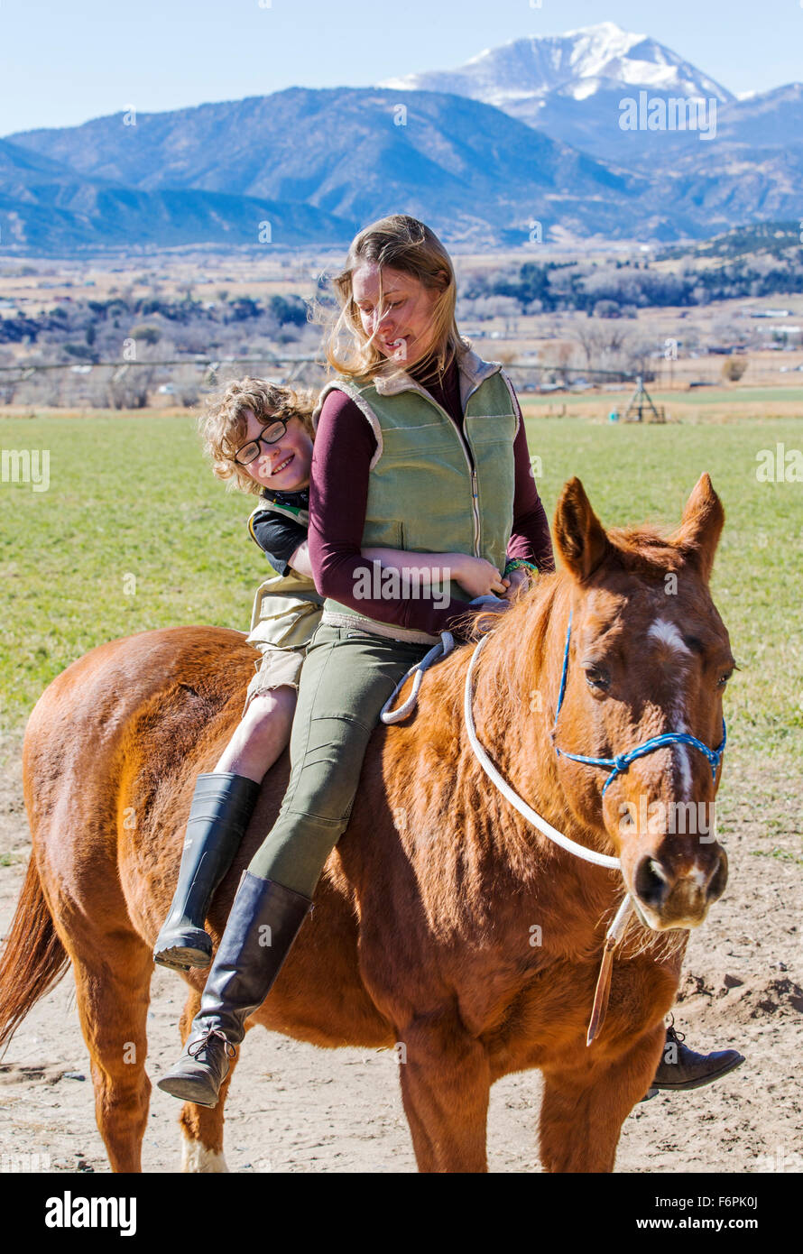Attractive mother and young son riding horse in ranch pasture Stock Photo