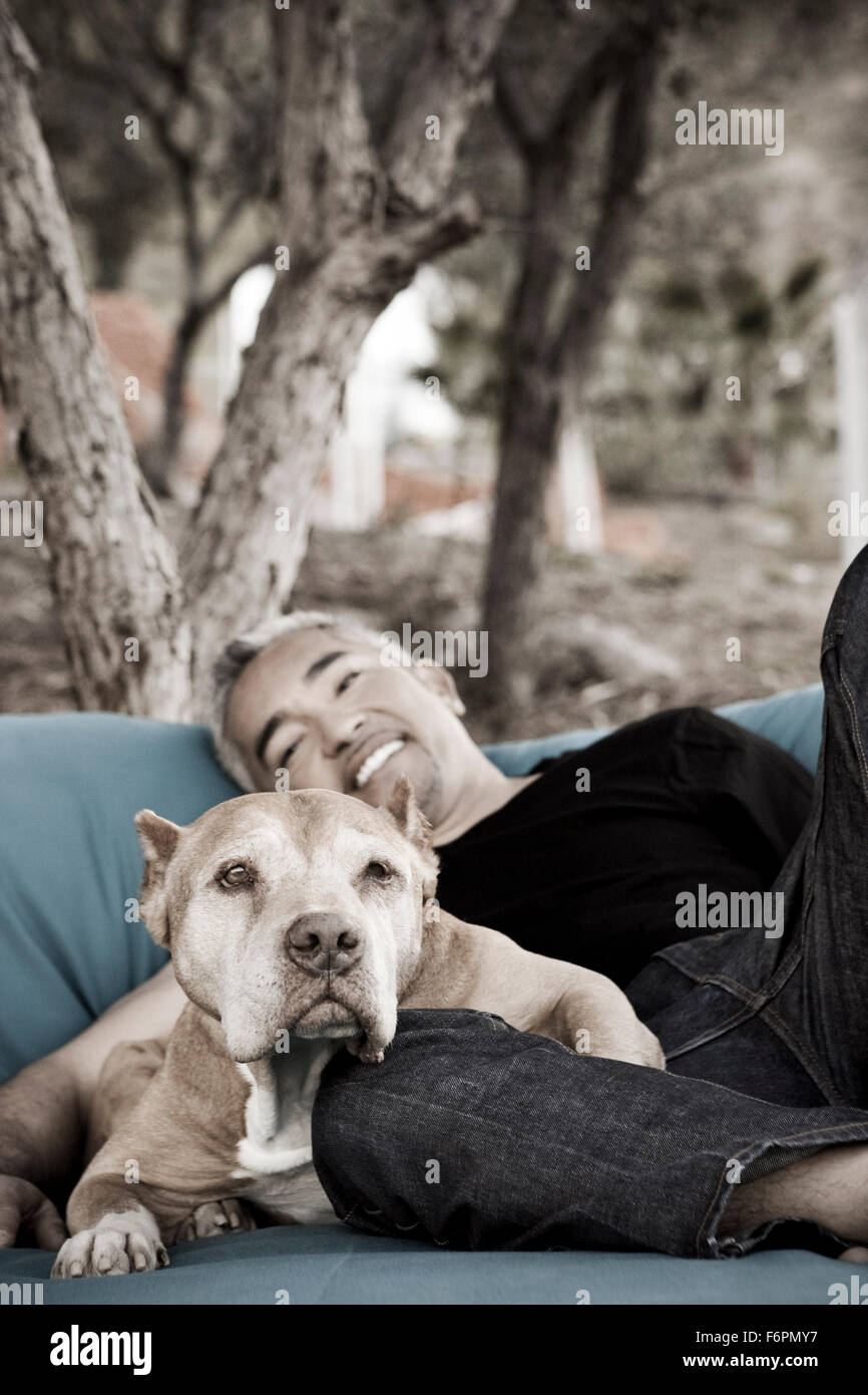Dog Whisperer Ceasr Millan at ranch shows love and affection laying down relaxing with pitbull dog Daddy on big lounge chair Stock Photo