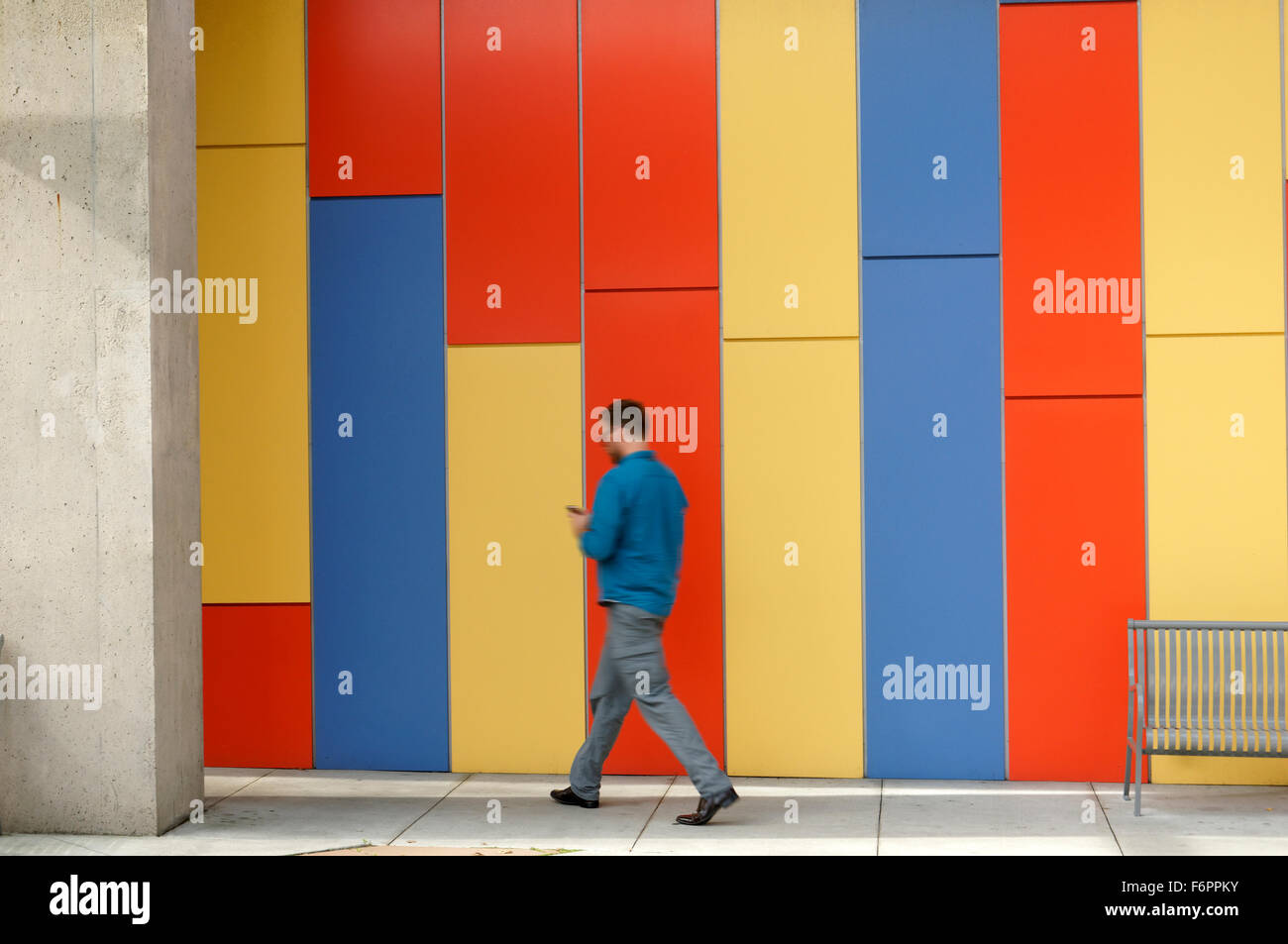Young adult man checking his cell phone while walking quickly past a colourful wall Stock Photo