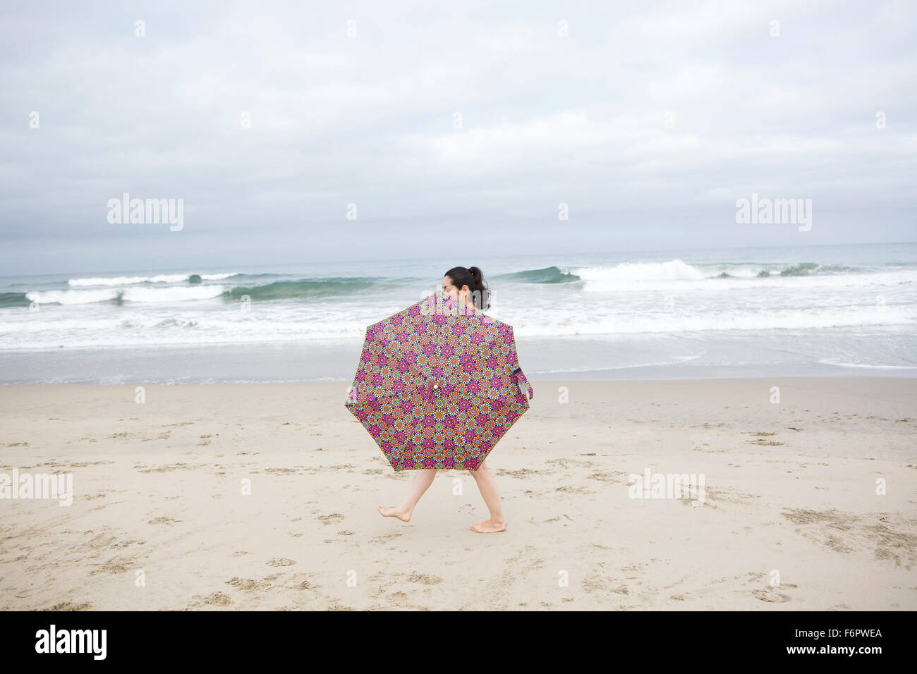 Woman walking with umbrella on beach Stock Photo