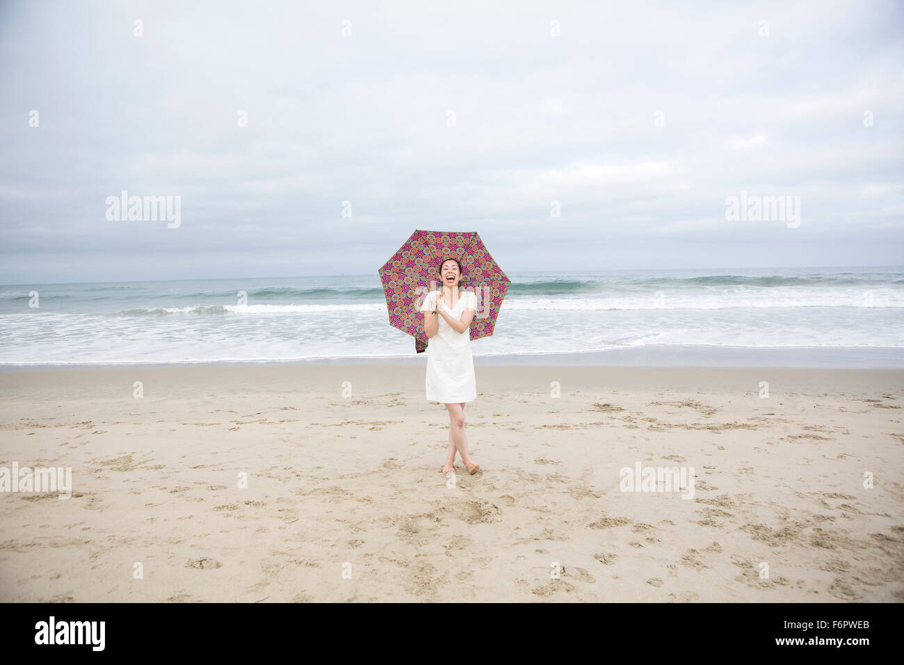 Woman laughing with umbrella on beach Stock Photo