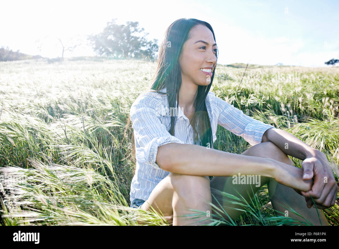 Mixed race woman sitting in field Stock Photo