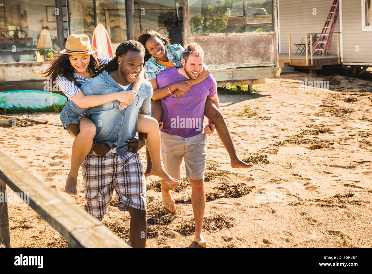 Men carrying girlfriends piggyback in sand Stock Photo