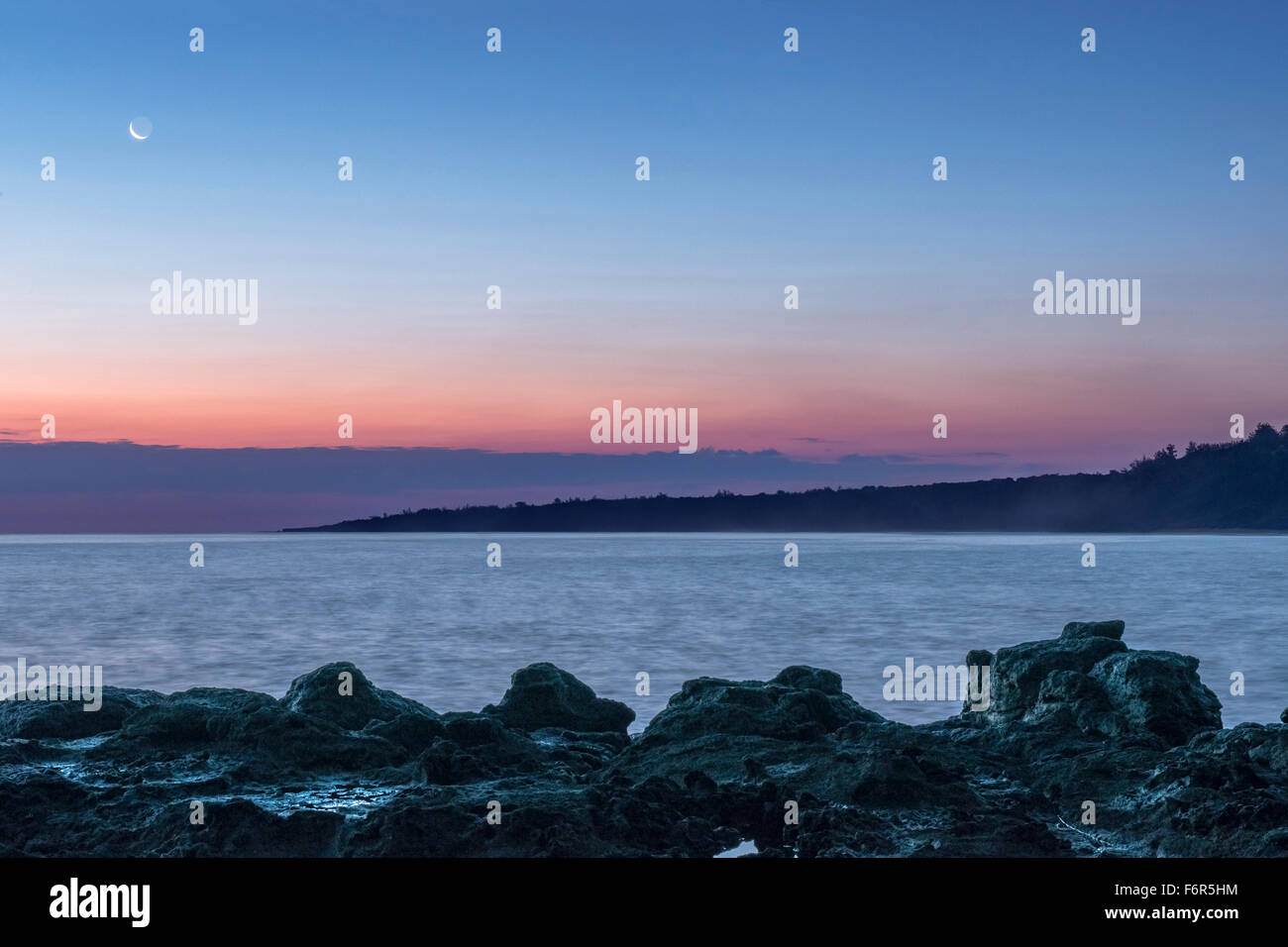 Sunrise over rock formations on beach Stock Photo