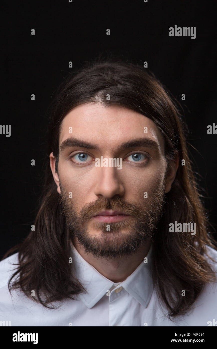 Portrait of a young man with beard and long hair looking at camera ...