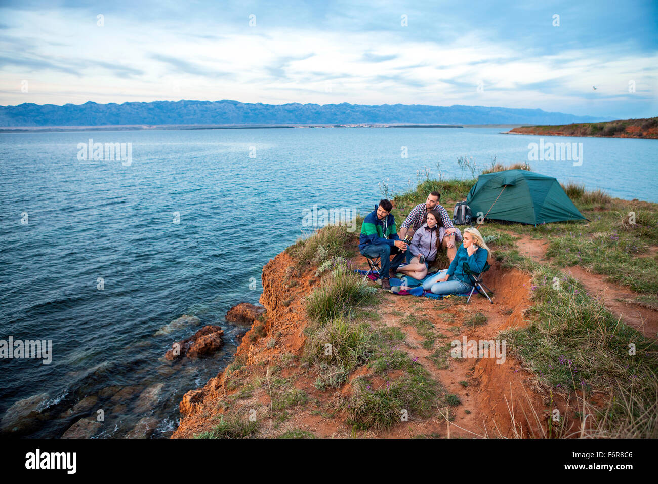 Group of friends sitting at campsite on water's edge Stock Photo