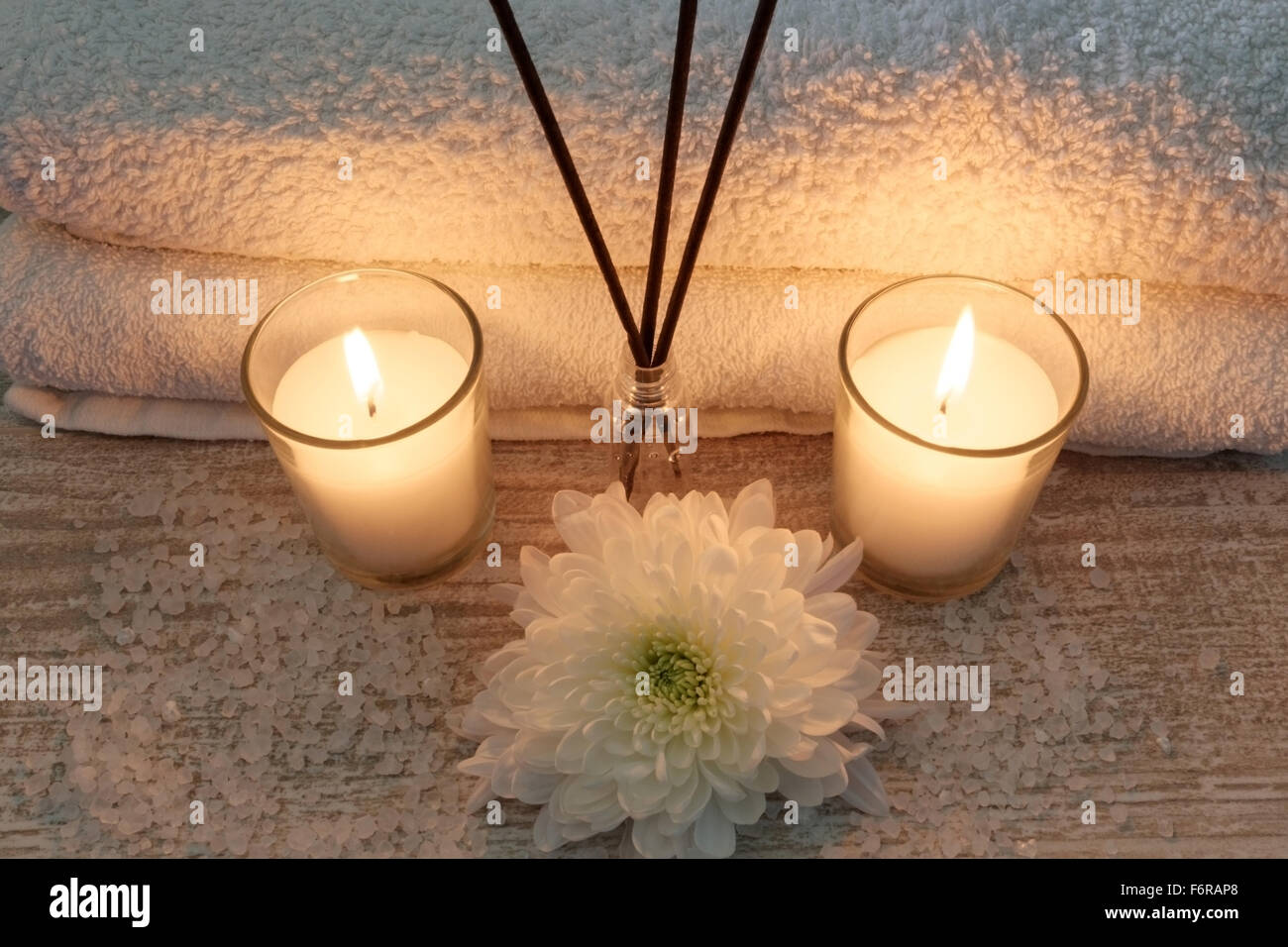 Spa composition with white towels, candles, flowers, incense sticks and bath salt on wooden table Stock Photo