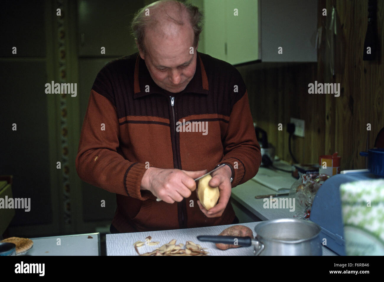Man peeling potatoes at the kitchen sink 1970's kitchen Stock Photo