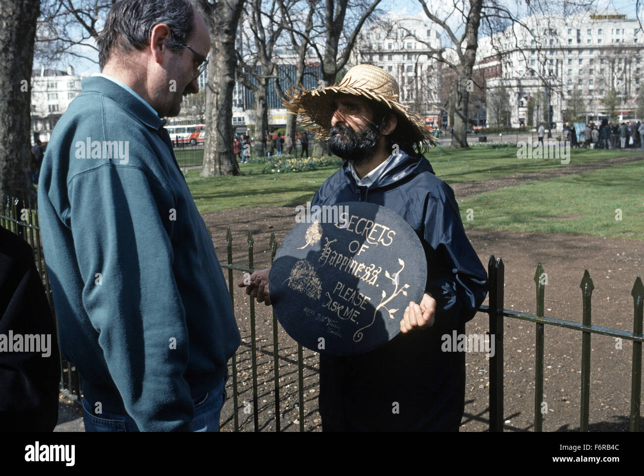 Man in straw hat at Speakers Corner in Hyde Park holding a sign saying Secrets of Happiness Ask Me another man present reading the sign Stock Photo