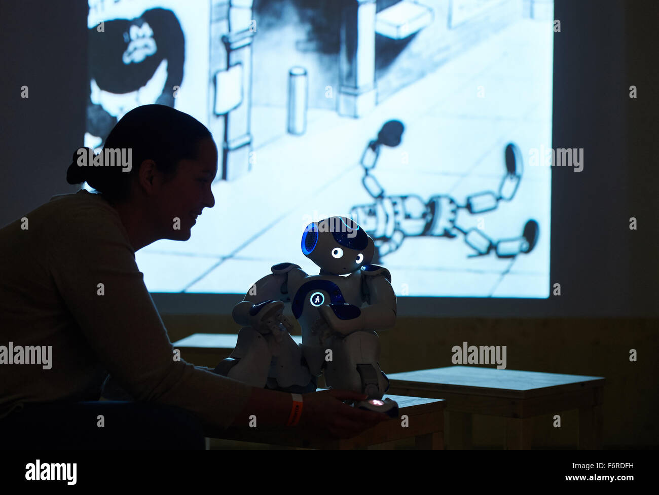 Dortmund, Germany. 19th Nov, 2015. Britta Grauel from the Federal Institute for Occupational Safety and Health demonstrates the robot 'NAO' while a Disney film plays in the background at the exhibition 'The Robots' in the DASA Working World Exhibition in Dortmund, Germany, 19 November 2015. The exhibition deals with the relationship between humans and machines and can be seen from 21 November 2015 until 25 September 2016. Photo: BERND THISSEN/dpa/Alamy Live News Stock Photo