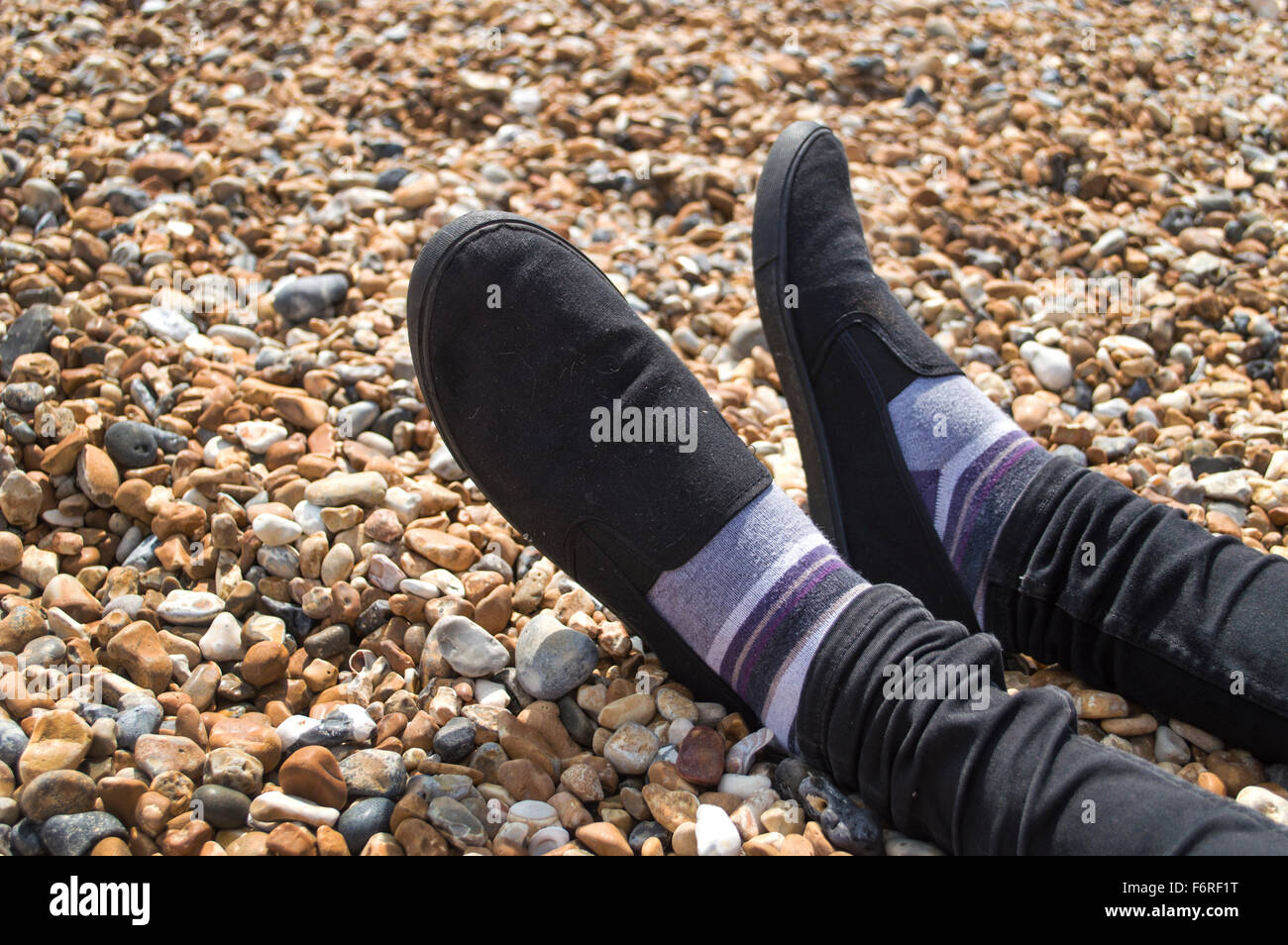 A pair of feet and legs, resting on the pebbles at Brighton's seafront. Stock Photo