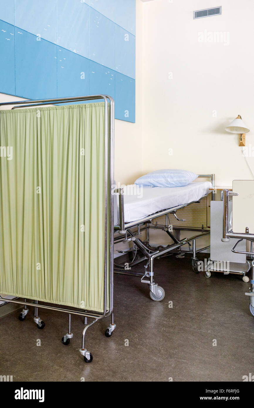 Close up of empty hospital bed behind bed screen in hospital ward with