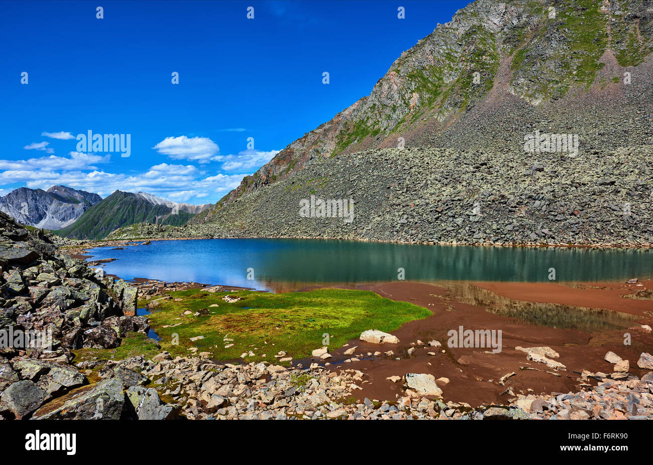 Patch of green grass on the edge of a mountain lake in a hanging valley between the rock fragments. Eastern Sayan. Buryatia Stock Photo