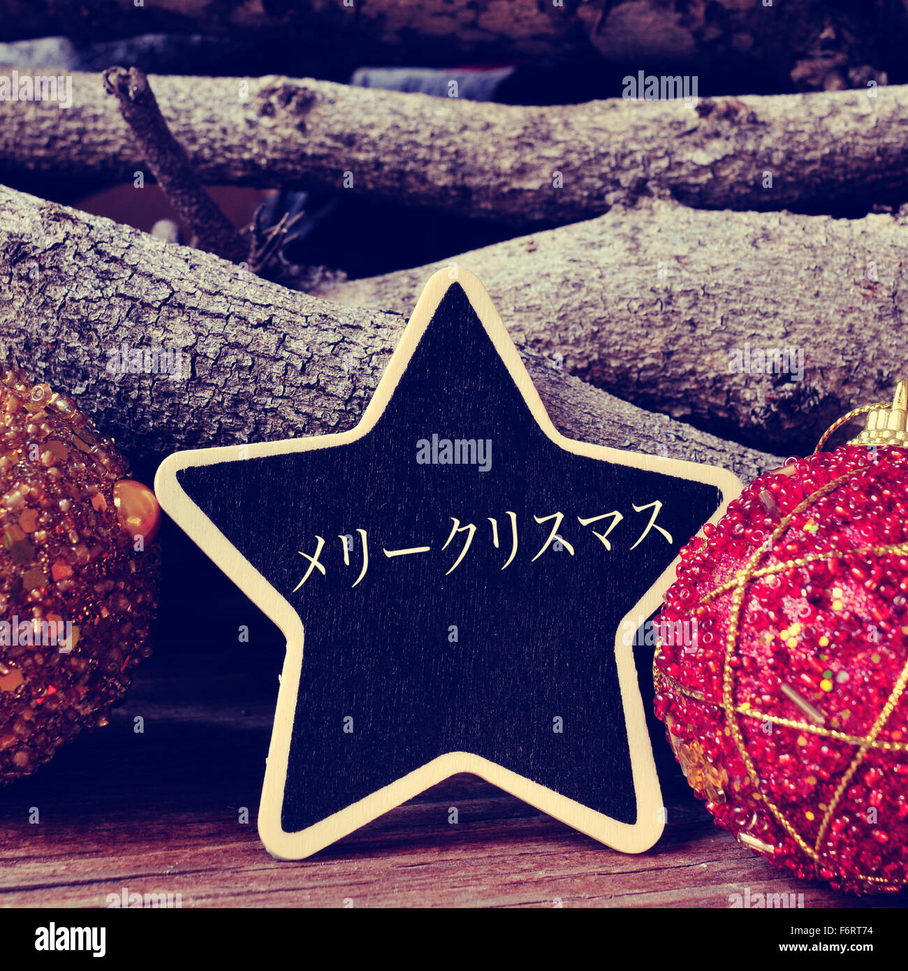 a star-shaped chalkboard with the text merry christmas written in japanese surrounded by christmas balls and logs Stock Photo