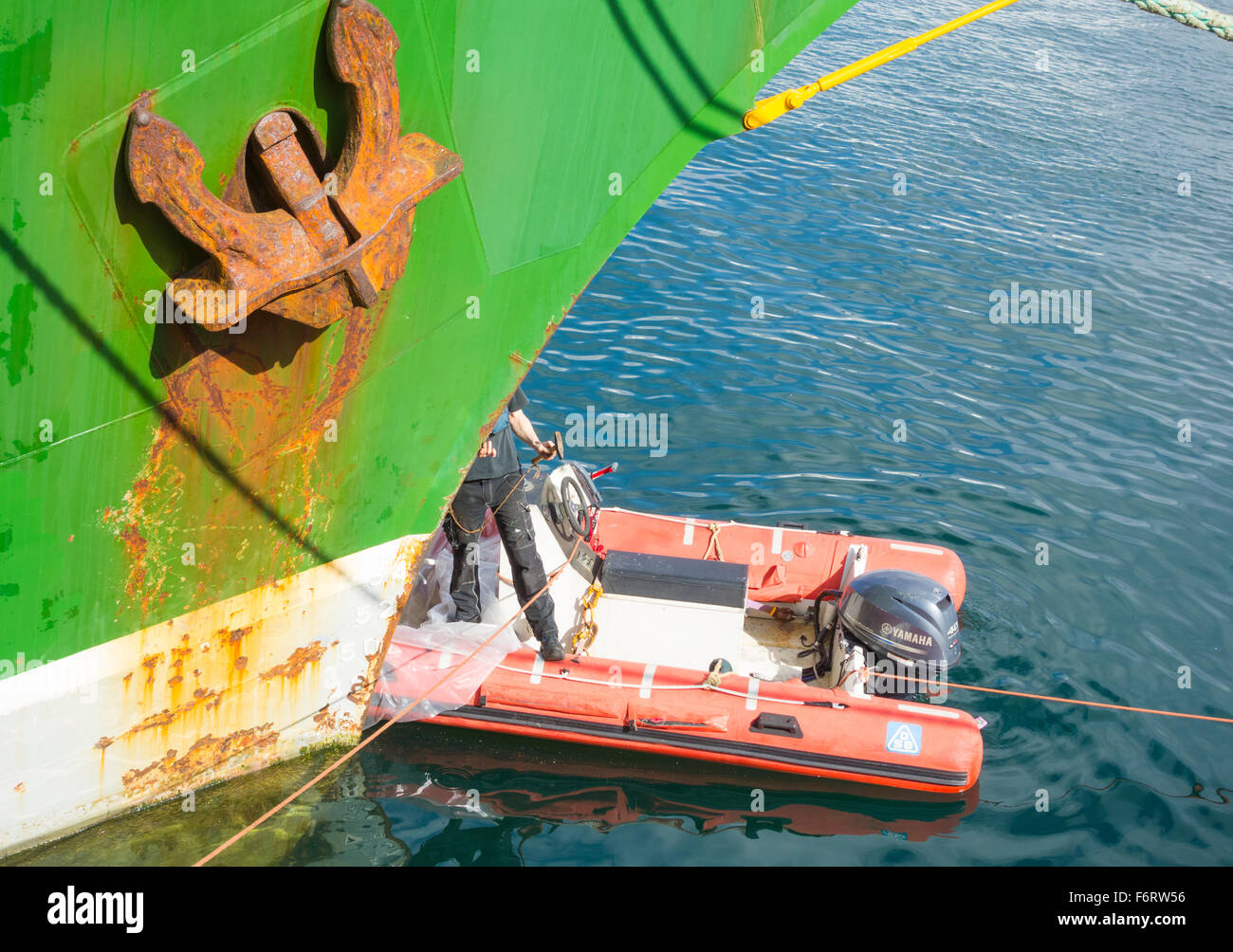 Standing in dinghy while removing rust from bow of Alexander von Humbold ship in Las Palmas port. Stock Photo