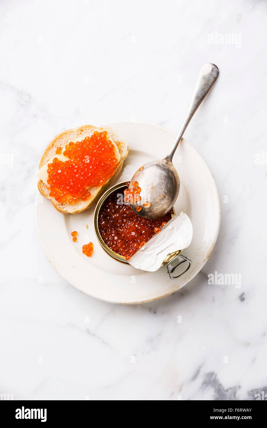 Salmon red caviar in can and sandwich on white marble background Stock Photo