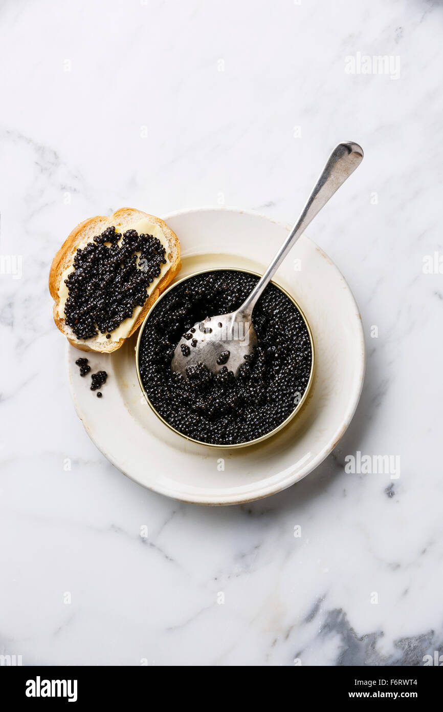 Sturgeon black caviar in can and sandwich on white marble background Stock Photo