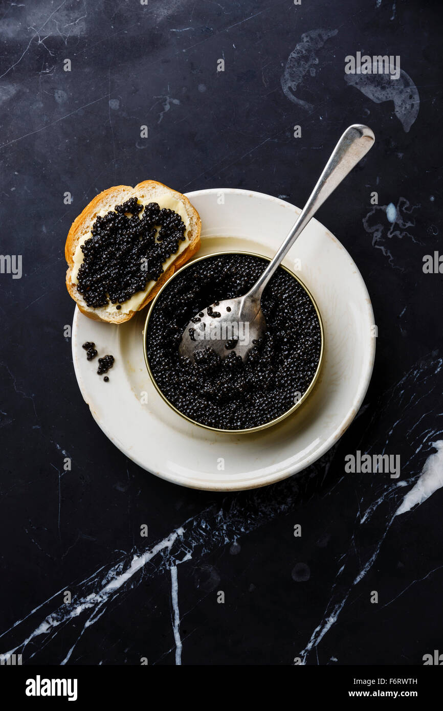 Sturgeon black caviar in can and sandwich on black marble background Stock Photo