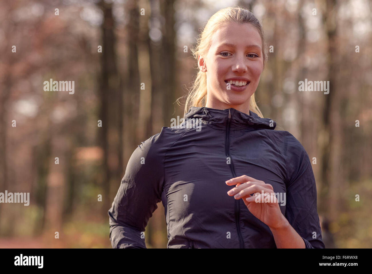 Pretty fit young woman jogging through autumn or fall woodland approaching the camera, close up upper body portrait in a healthy Stock Photo