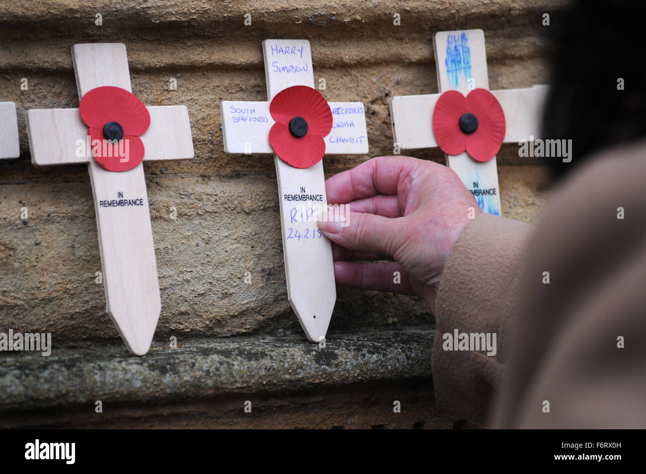 PERSON PLACING REMEMBRANCE DAY POPPY CROSS ON WAR MEMORIAL RE WAR POPPIES BRITISH LEGION FALLEN SOLDIERS FIRST WORLD WAR DIED UK Stock Photo