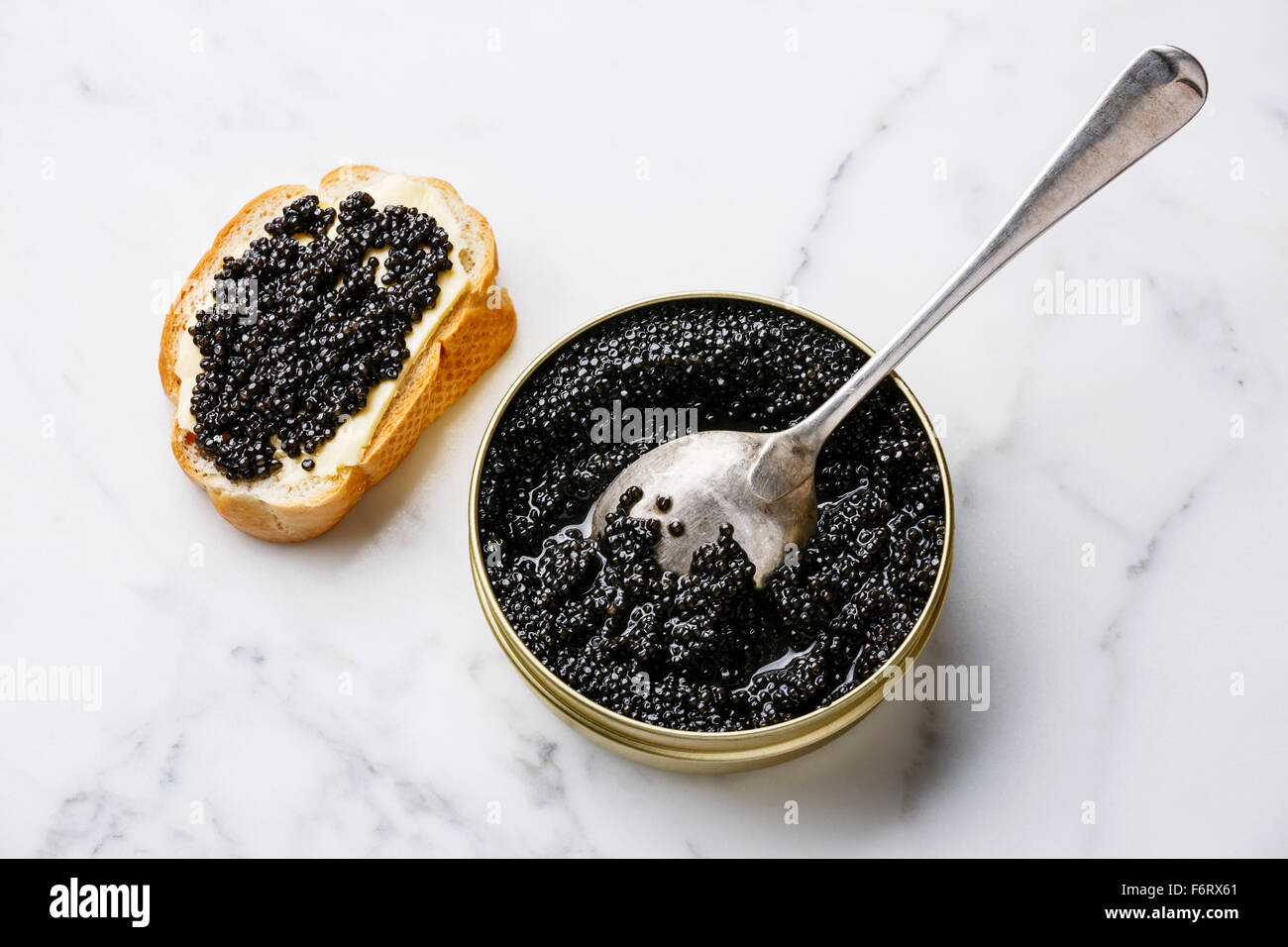 Sturgeon black caviar in can and sandwich on white marble background Stock Photo