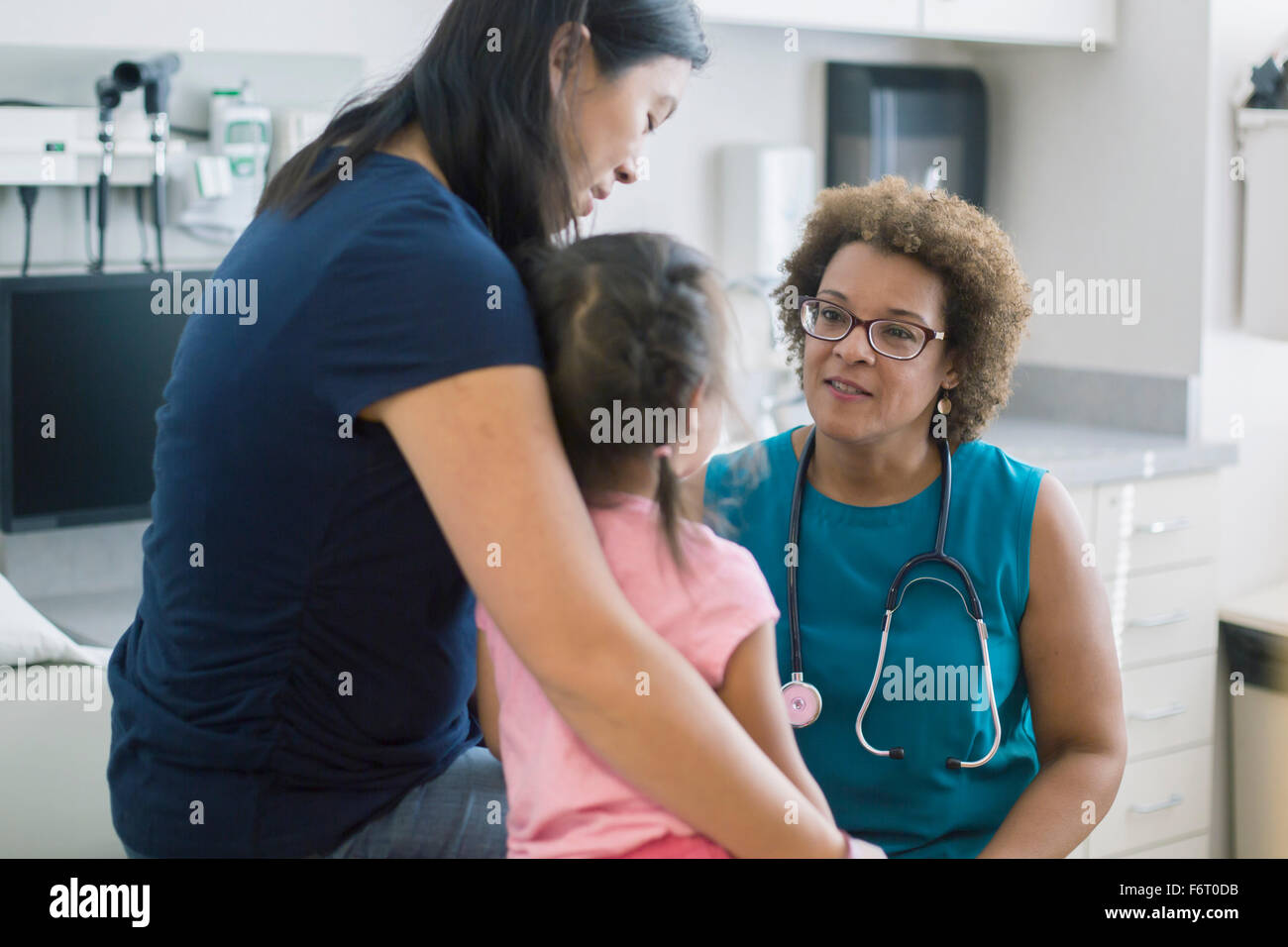 Doctor talking to mother and daughter in hotel room Stock Photo