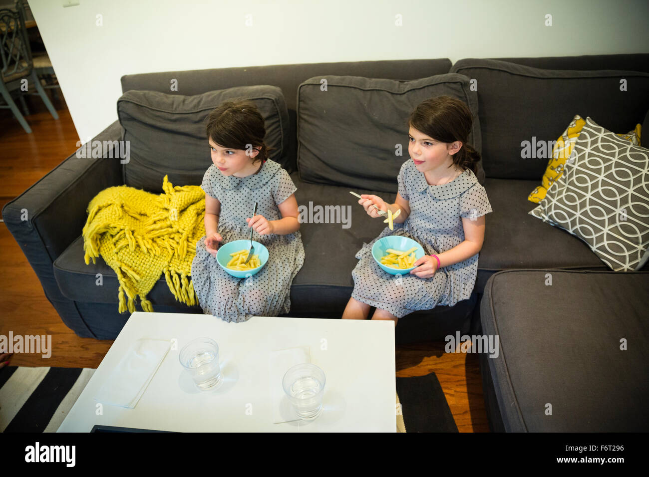 Twin sisters eating on sofa Stock Photo