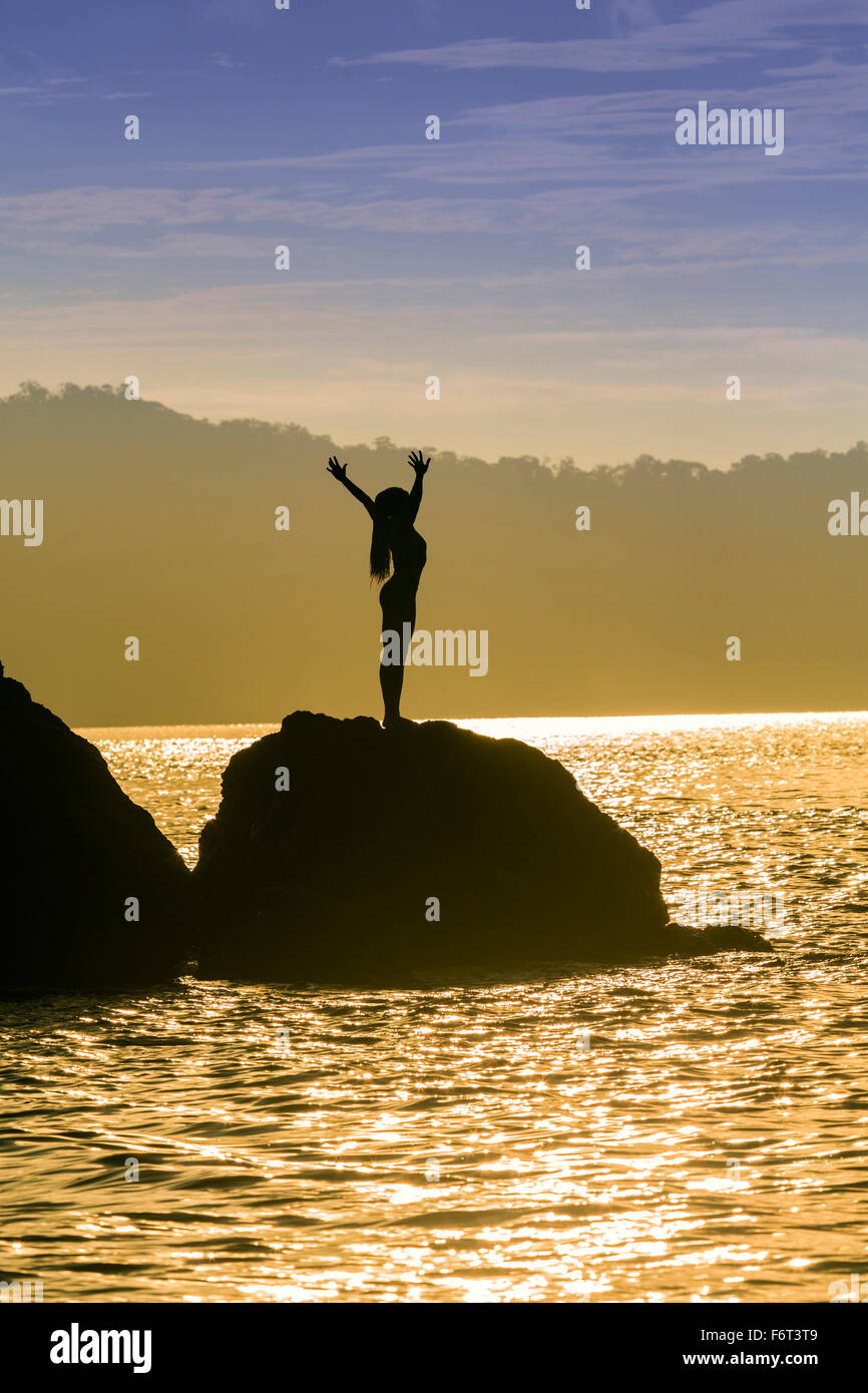 Mixed race woman standing on rock over ocean Stock Photo