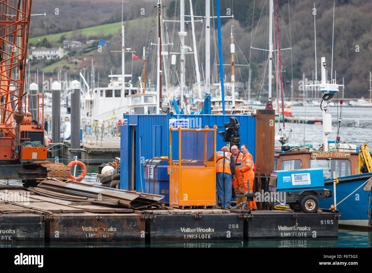 Workmen wearing 'hi-viz' clothing work on a floating construction platform work in Dartmouth harbour. Stock Photo