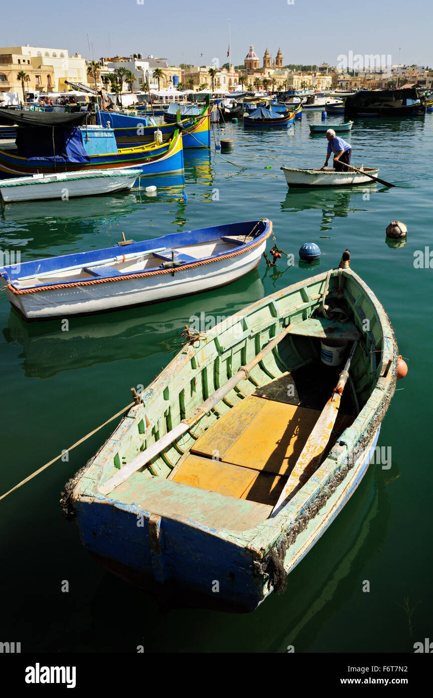 Old man standing on a small boat with many other boats around in the port of Marsaxlokk, Malta Stock Photo