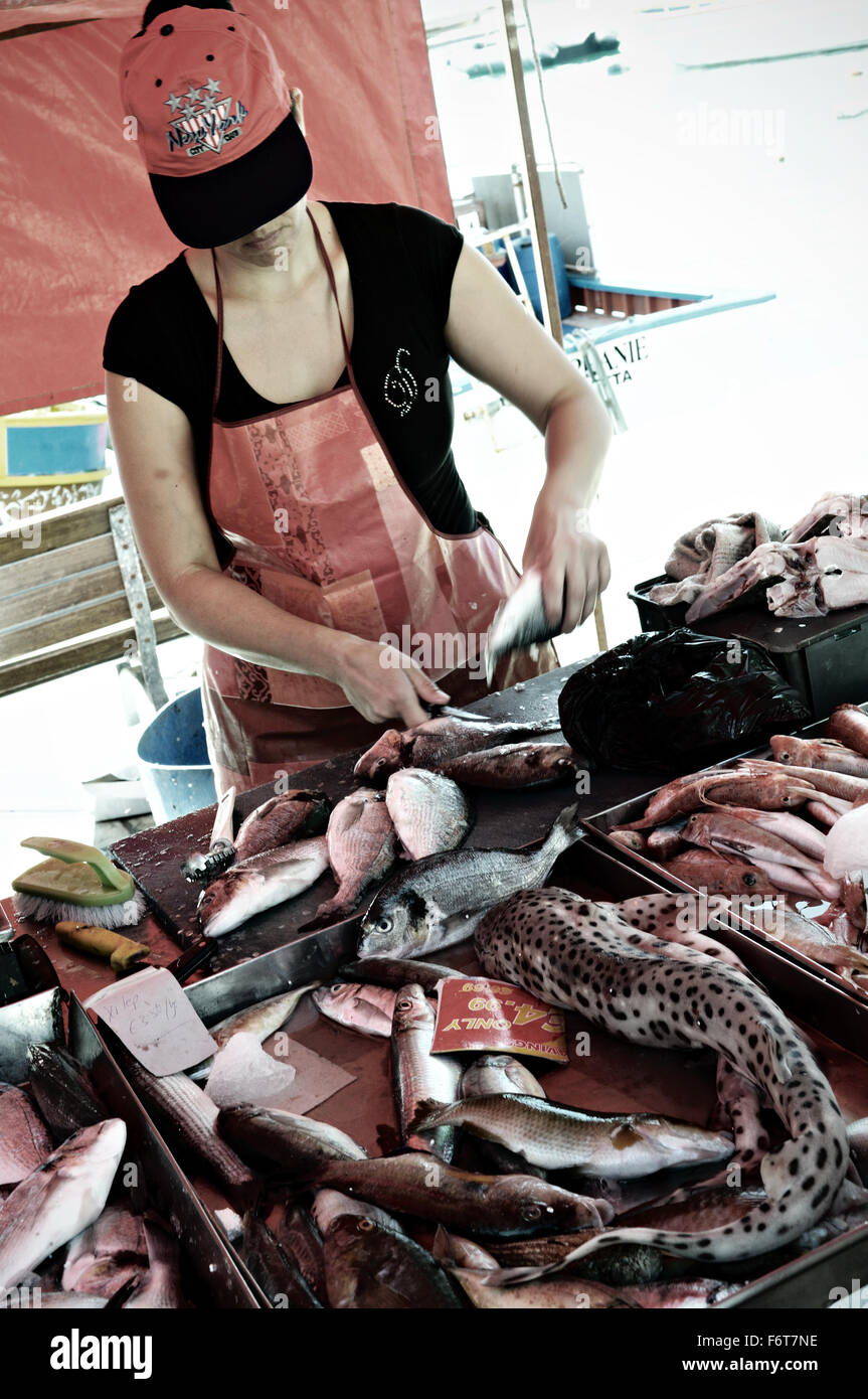 Woman with a red cap cutting fish at the fish market of Marsaxlokk, Malta Stock Photo