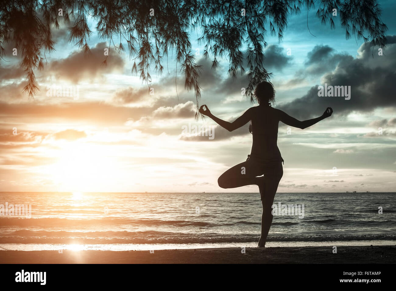 Silhouette of woman standing at yoga pose on the beach during sunset in ...