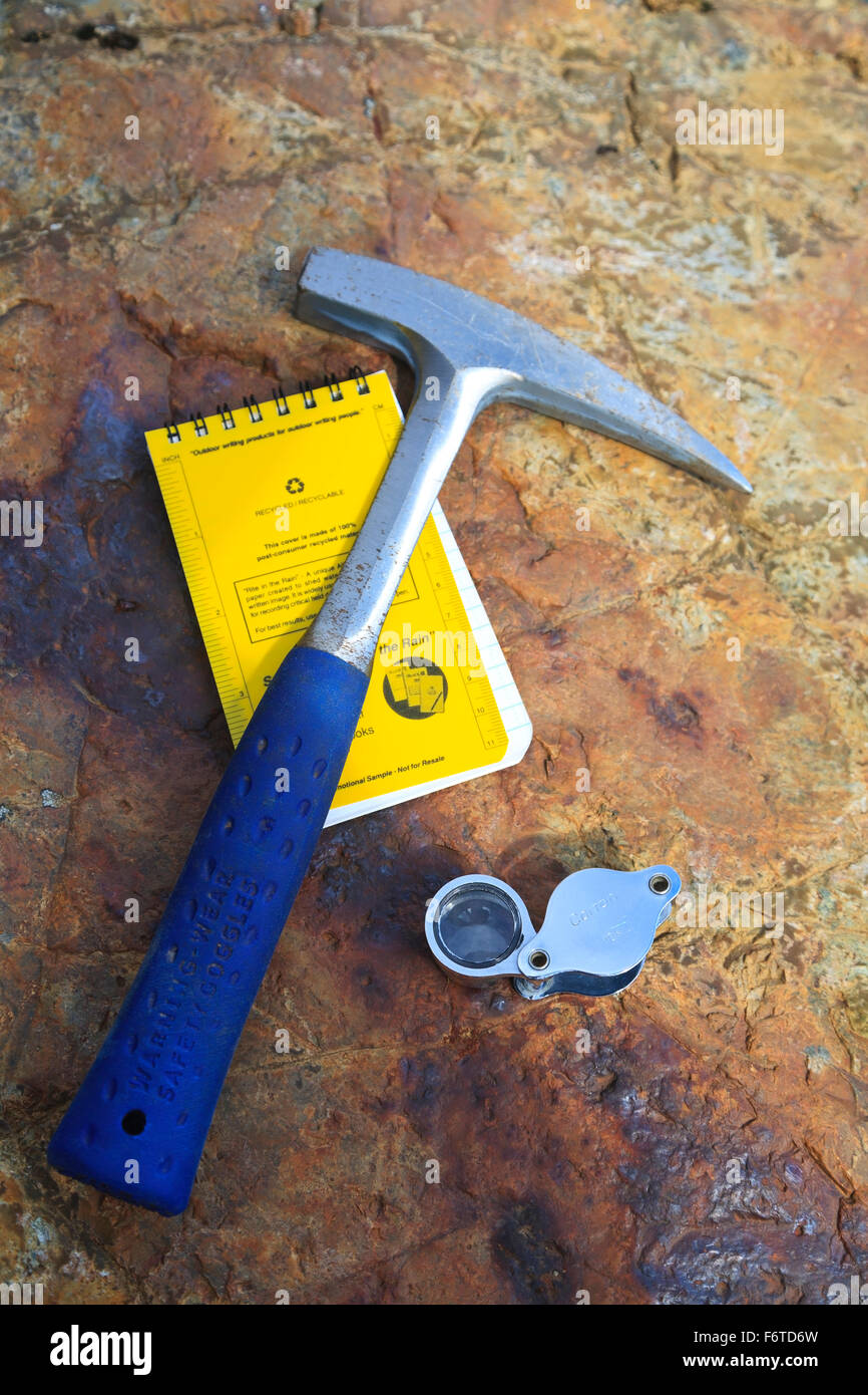 Mineral exploration with rock hammer, notebook, and magnifying glass on mineral stained rock background, Smithers, British Colum Stock Photo