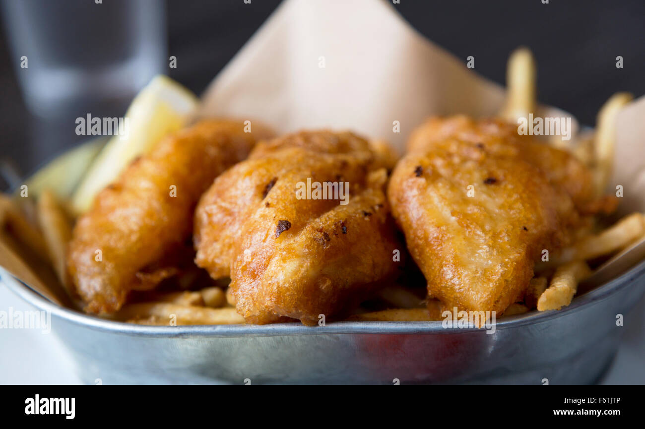 Casual fried fish placed on fried potatoes in metal dish. Stock Photo