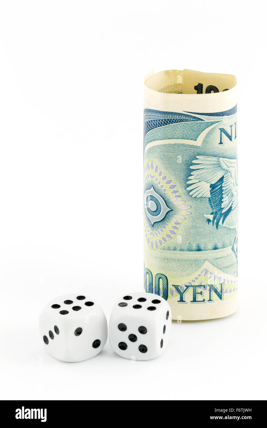 Yen currency stands next to pair of dice on white background in vertical image with copy space. Stock Photo