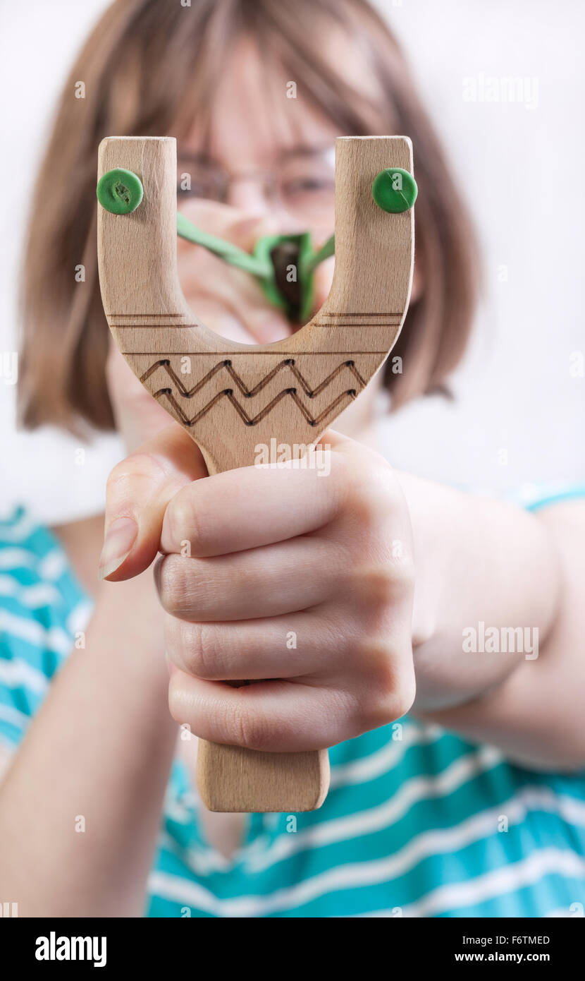 direct view of girl pulling green rubber band of simple wooden slingshot Stock Photo