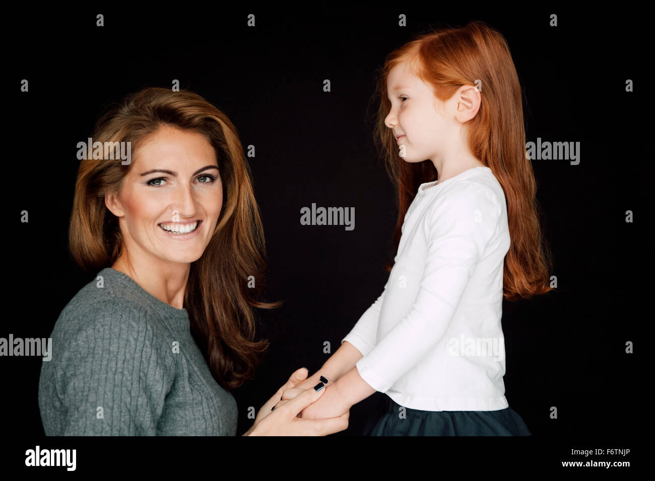 Mother and little daughter holding hands in front of black background ...
