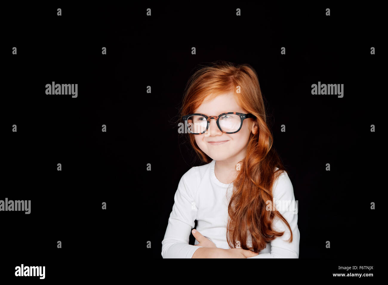 Portrait of redheaded smiling little girl wearing oversized glasses in front of black background Stock Photo