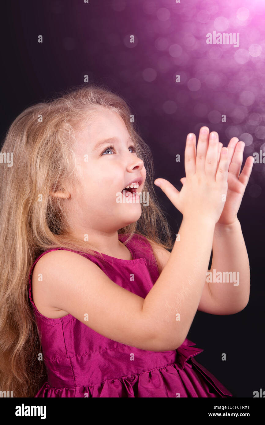 Little cute girl in a pink dress on a black background in the studio ...