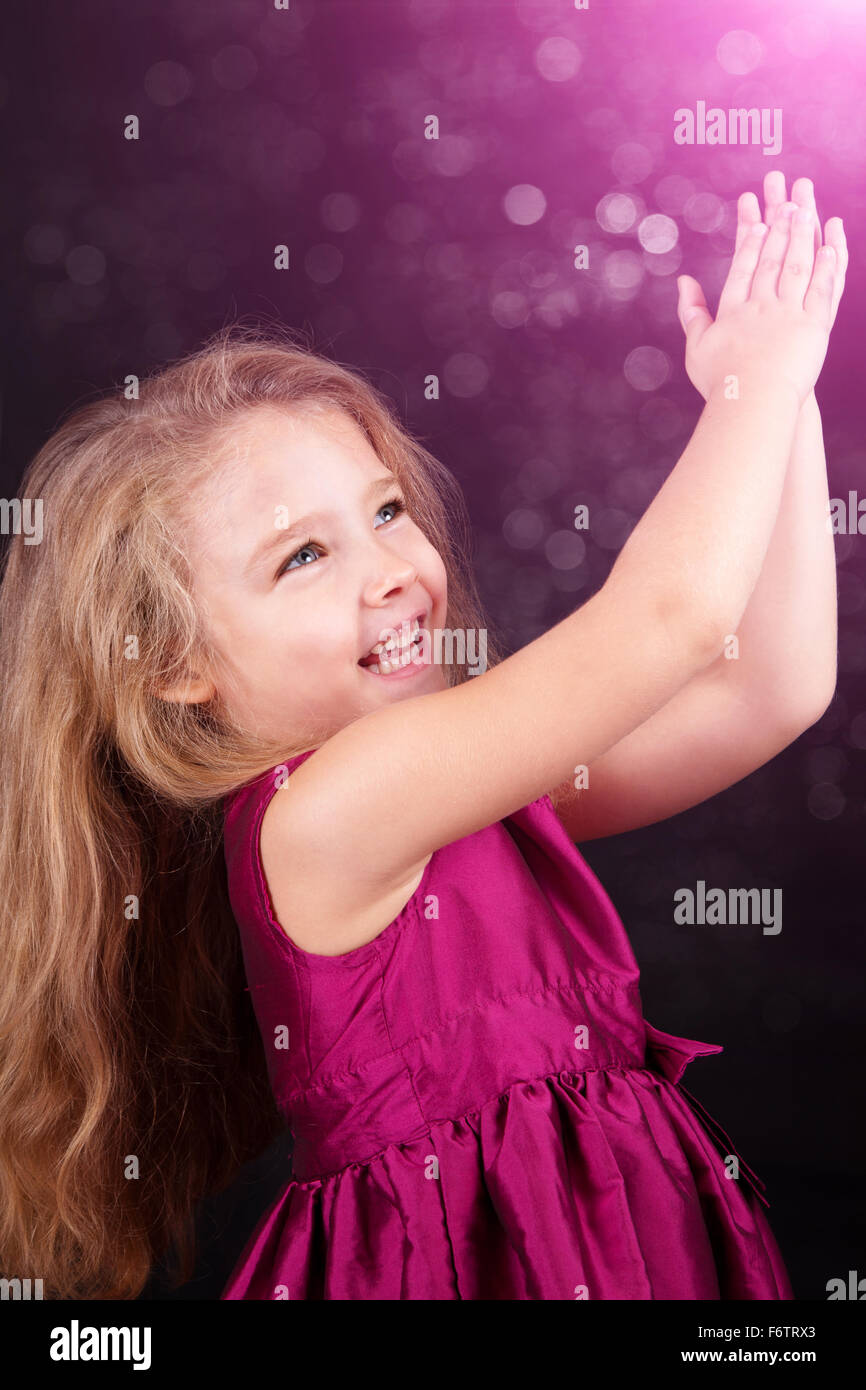 Little cute girl in a pink dress on a black background in the studio ...