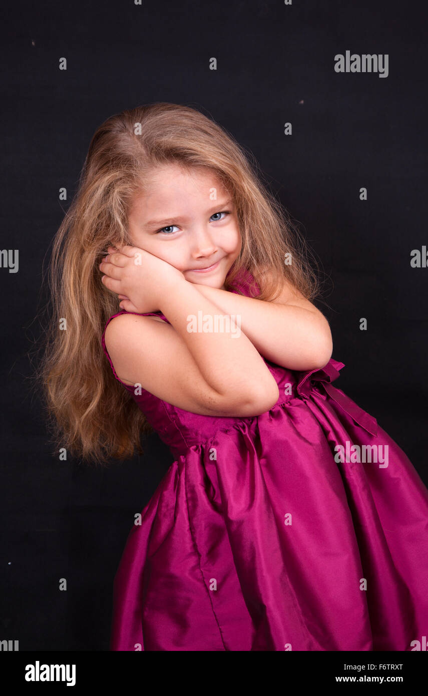 Little cute girl in a pink dress on a black background in the studio ...