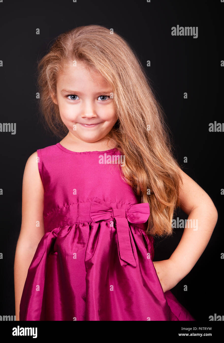 Little cute girl in a pink dress on a black background in the studio ...