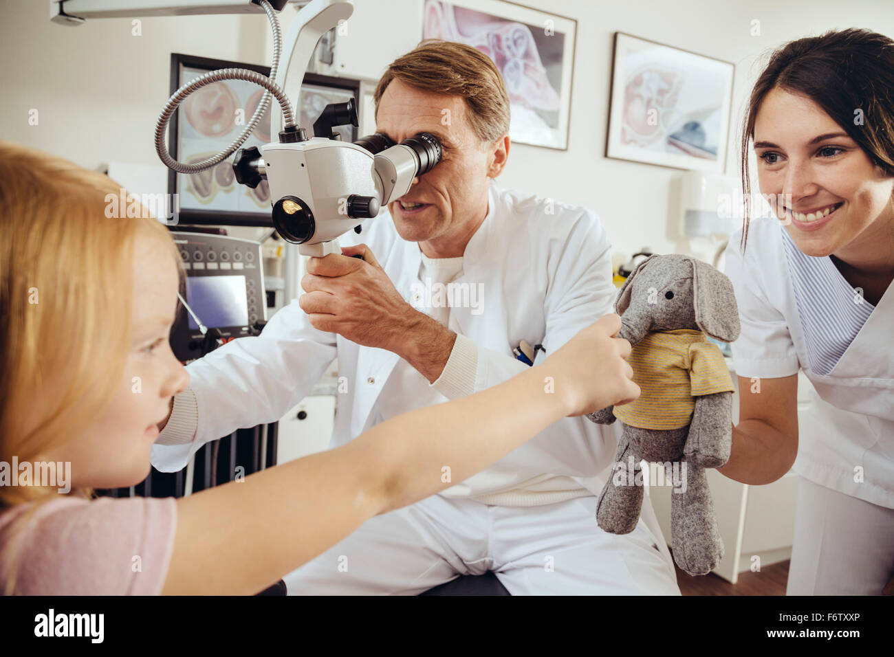 Nurse distracting child with toy while doctor using surgical microscope to check ears Stock Photo