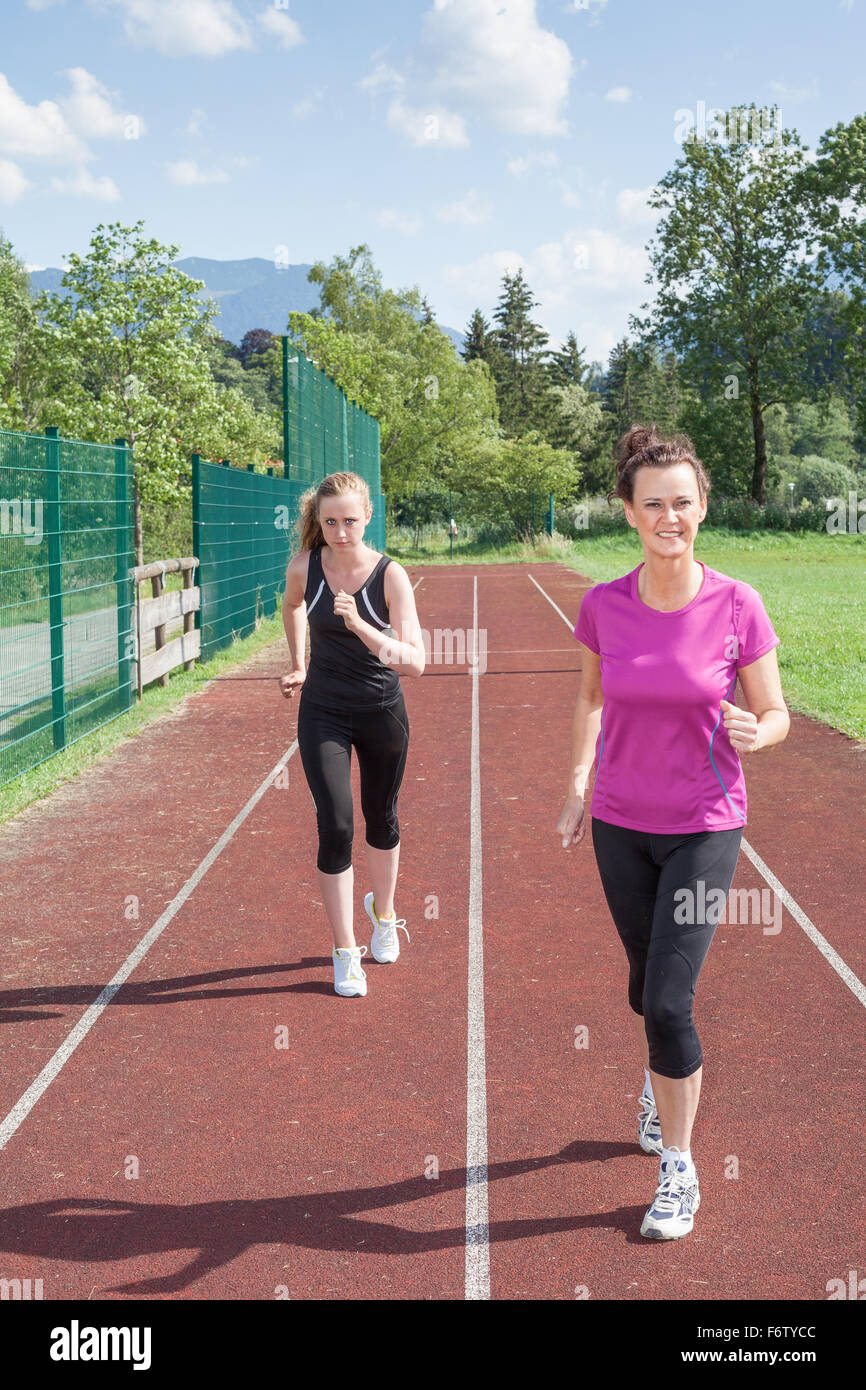 Two Women Running on Track Together and Having Friendly Race - Confident Brunette Woman Beating Blond Woman in Track Race Stock Photo